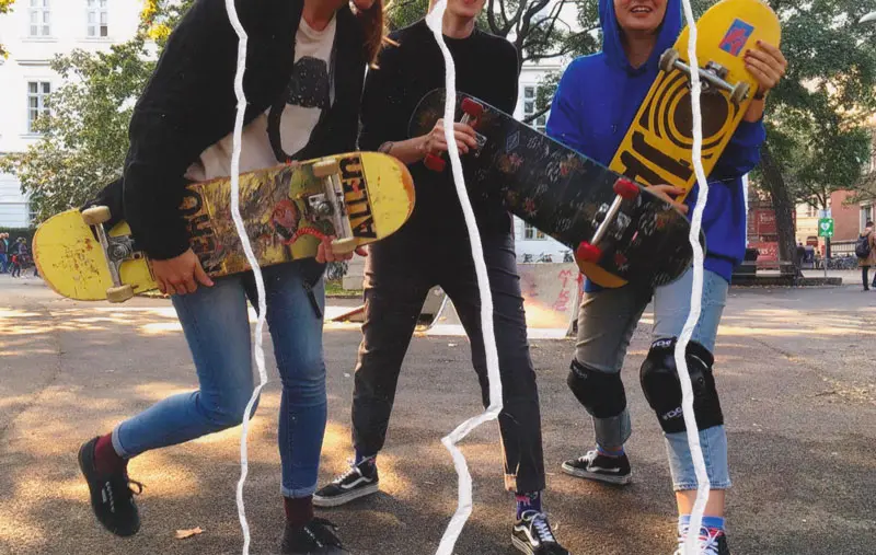 3 Skateboarder:innen halten ihre Skateboards in die Höhe.