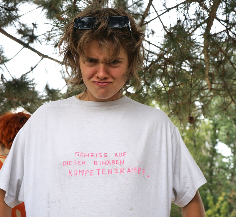 Jojo mit weißem T-Shirt. Aufschrift „Scheiss auf diesen binären Kompetenzkampf“